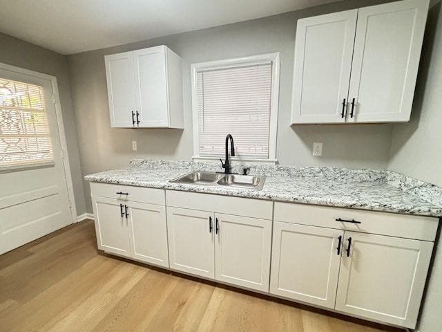 kitchen with white cabinets, light stone counters, a sink, light wood-style flooring, and baseboards