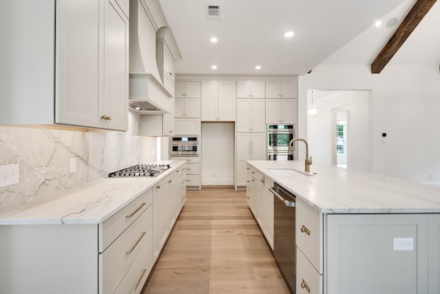 kitchen with visible vents, appliances with stainless steel finishes, a sink, custom range hood, and light wood-style flooring