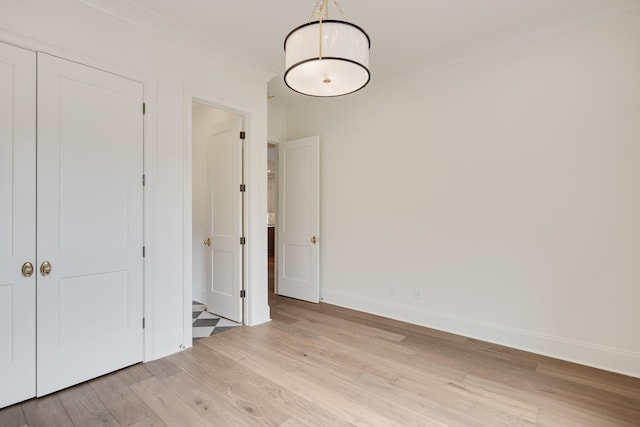 unfurnished bedroom with baseboards, ornamental molding, light wood-style flooring, and a closet