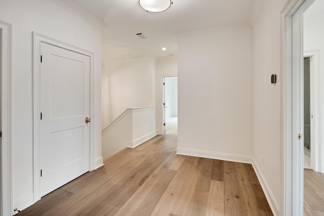 corridor featuring baseboards, ornamental molding, light wood-style flooring, and visible vents