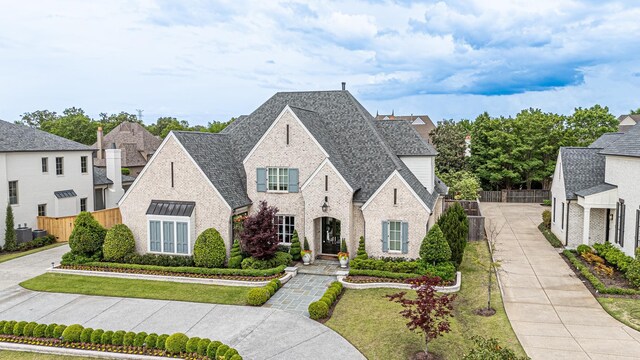 view of front of house featuring fence, brick siding, and roof with shingles