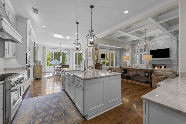 kitchen featuring a sink, under cabinet range hood, appliances with stainless steel finishes, a chandelier, and open floor plan