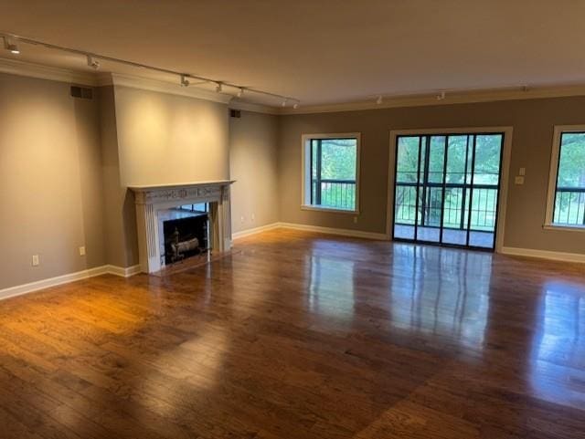 unfurnished living room with rail lighting, dark wood finished floors, ornamental molding, and baseboards