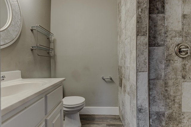 bathroom with vanity, wood finished floors, toilet, baseboards, and tiled shower