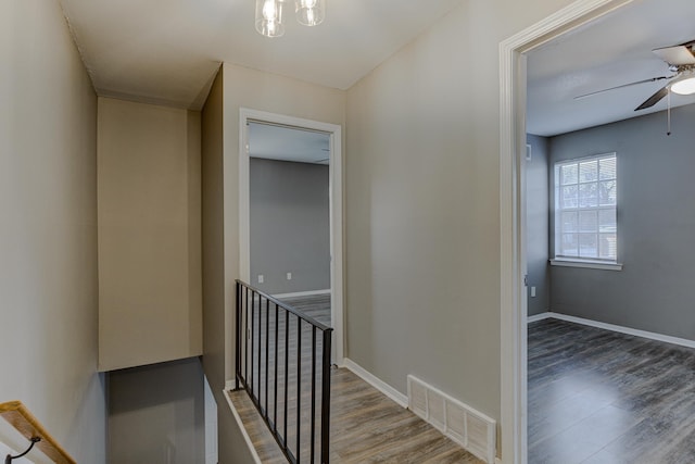 corridor featuring baseboards, visible vents, wood finished floors, and an upstairs landing