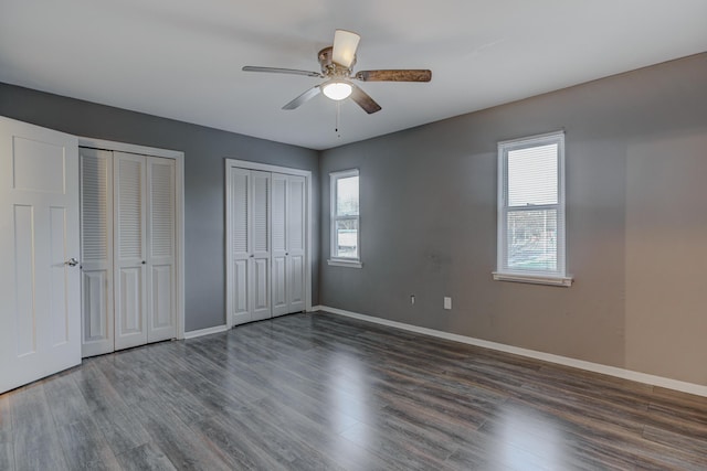 unfurnished bedroom with two closets, multiple windows, and wood finished floors
