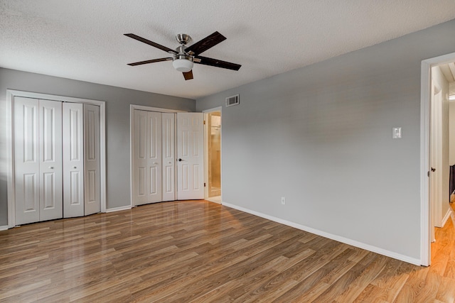 unfurnished bedroom featuring baseboards, two closets, wood finished floors, and visible vents