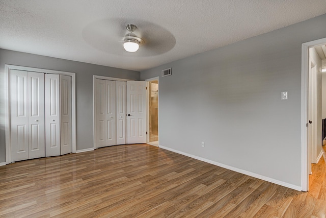 unfurnished bedroom featuring multiple closets, baseboards, light wood-type flooring, and visible vents