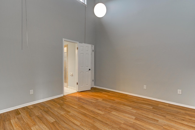 spare room with baseboards, light wood-style flooring, and a towering ceiling