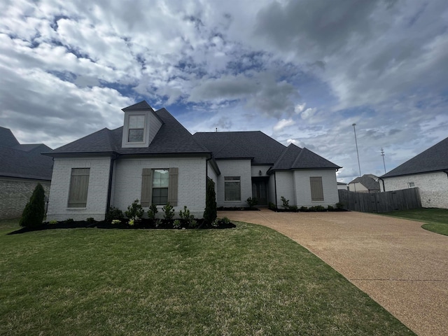 view of front of property featuring brick siding, fence, a front yard, and roof with shingles