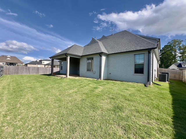rear view of property with a lawn, brick siding, cooling unit, a fenced backyard, and a shingled roof