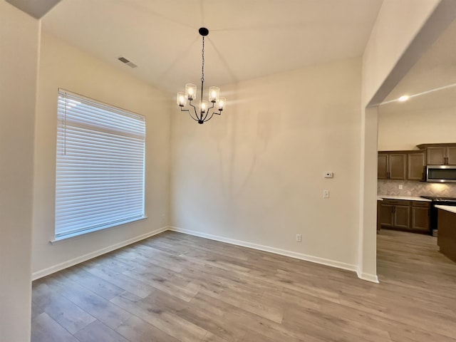 unfurnished dining area featuring plenty of natural light, visible vents, light wood-type flooring, baseboards, and a chandelier