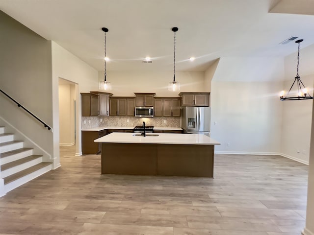 kitchen featuring baseboards, an island with sink, light countertops, backsplash, and stainless steel appliances