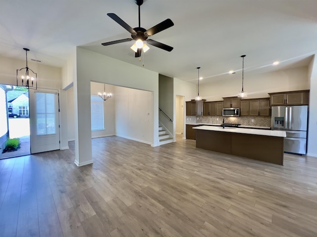 unfurnished living room featuring stairway, baseboards, ceiling fan with notable chandelier, and light wood-type flooring