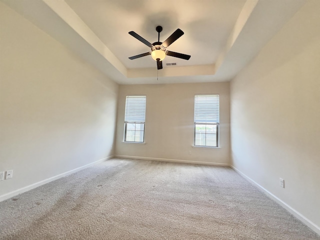 carpeted empty room featuring baseboards, a ceiling fan, a tray ceiling, and a wealth of natural light