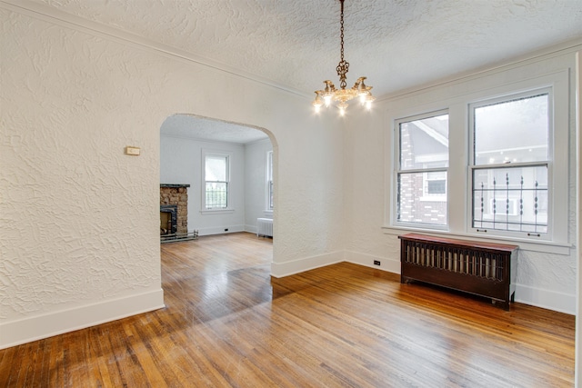 unfurnished dining area with a textured ceiling, arched walkways, wood finished floors, baseboards, and radiator