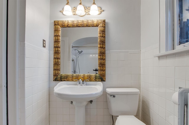 bathroom with tile walls, wainscoting, toilet, and a shower
