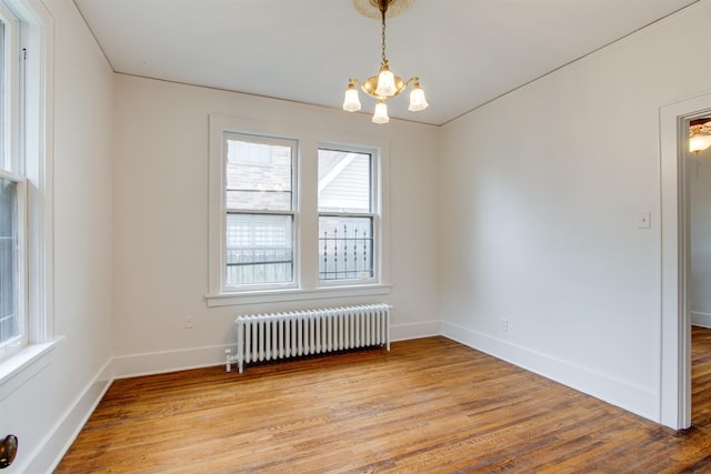 unfurnished room with baseboards, a notable chandelier, radiator heating unit, and light wood finished floors