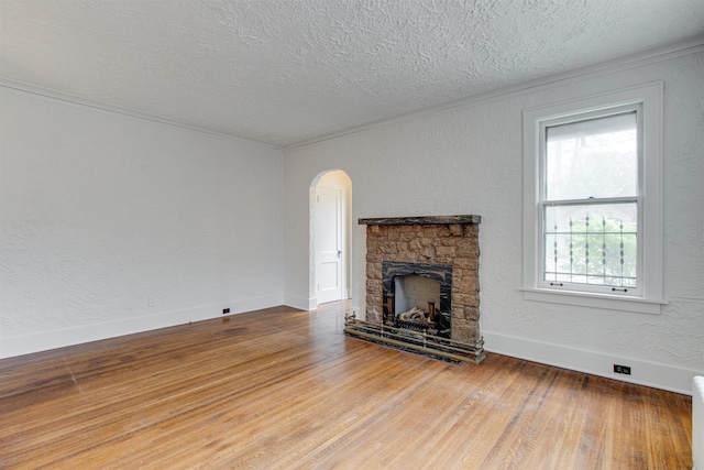 unfurnished living room with a textured wall, arched walkways, a textured ceiling, a stone fireplace, and wood finished floors