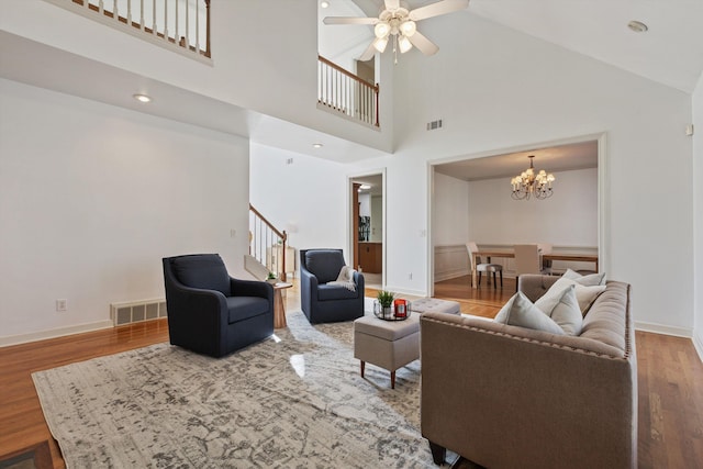 living area with visible vents, wood finished floors, high vaulted ceiling, ceiling fan with notable chandelier, and stairs