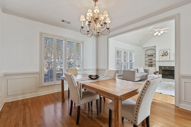 dining area with visible vents, built in features, a fireplace, light wood-style flooring, and vaulted ceiling