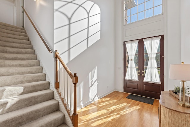 foyer featuring a high ceiling, french doors, baseboards, light wood-type flooring, and stairway