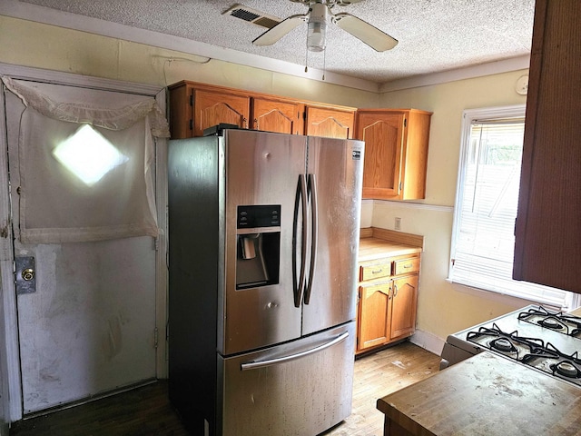 kitchen featuring visible vents, light wood-style floors, gas range, stainless steel fridge with ice dispenser, and a ceiling fan