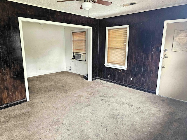 carpeted spare room with visible vents, a ceiling fan, a textured ceiling, and wooden walls