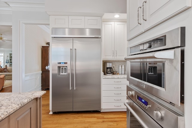 kitchen featuring wainscoting, stainless steel appliances, ornamental molding, and light wood-type flooring