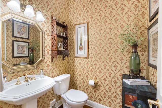 bathroom with baseboards, toilet, wallpapered walls, and a sink