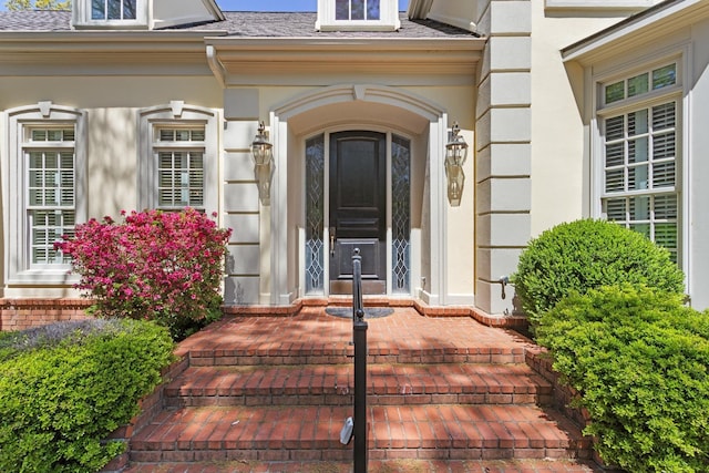 doorway to property with a porch, a shingled roof, and stucco siding