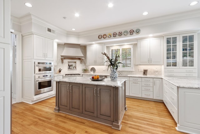 kitchen with stainless steel double oven, visible vents, premium range hood, glass insert cabinets, and white cabinetry