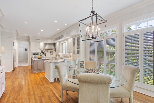 dining space featuring an inviting chandelier, ornamental molding, light wood-style flooring, and a wealth of natural light
