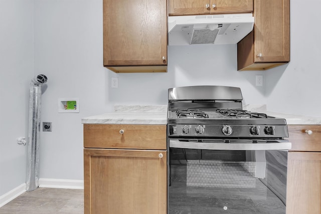 kitchen with baseboards, light countertops, under cabinet range hood, and stainless steel gas stove