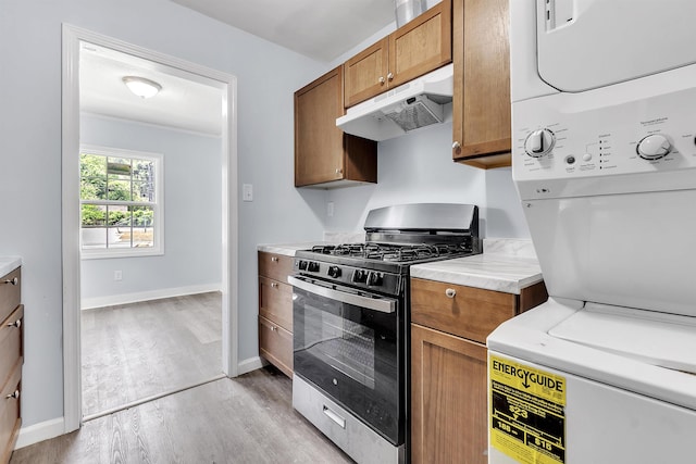 kitchen with stacked washer and dryer, light wood-style floors, light countertops, stainless steel range with gas cooktop, and under cabinet range hood