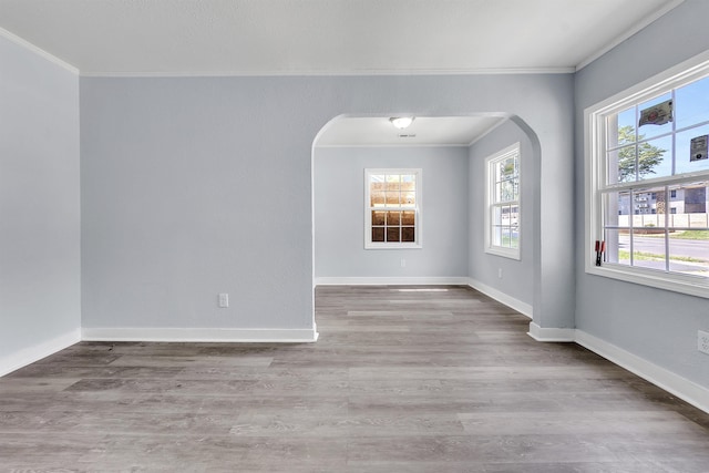 empty room featuring crown molding, arched walkways, and wood finished floors