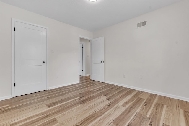 empty room with baseboards, visible vents, and light wood finished floors