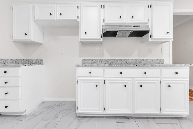 kitchen with under cabinet range hood, white cabinetry, light stone countertops, and marble finish floor
