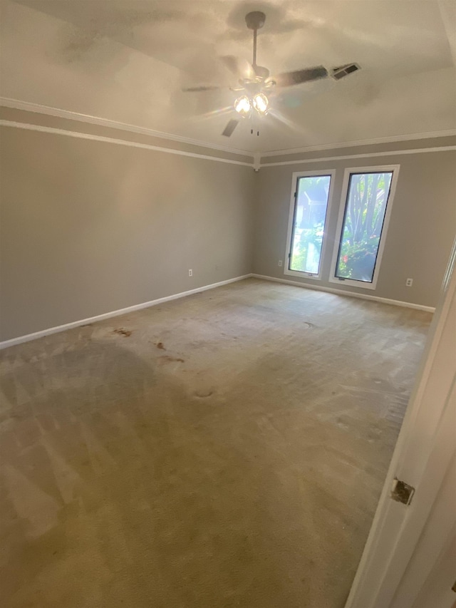 empty room with a ceiling fan, light colored carpet, crown molding, visible vents, and baseboards