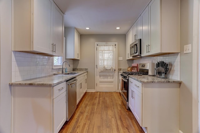 kitchen featuring appliances with stainless steel finishes, light stone countertops, light wood-type flooring, a sink, and recessed lighting