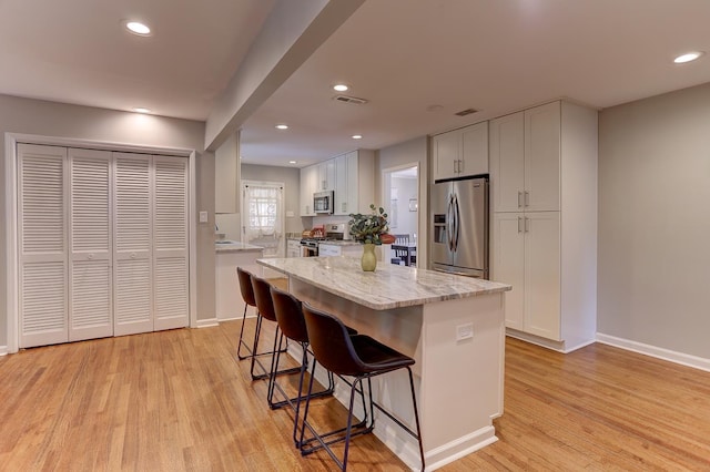 kitchen with appliances with stainless steel finishes, light stone counters, light wood finished floors, a breakfast bar area, and baseboards