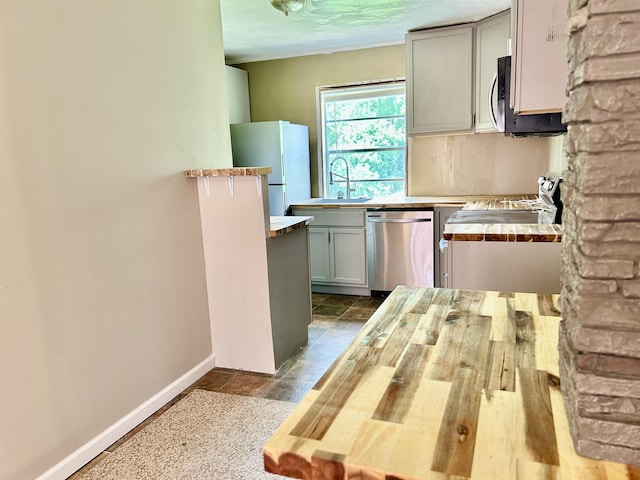 kitchen with a sink, baseboards, gray cabinets, and stainless steel appliances