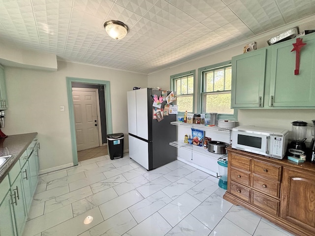 kitchen featuring freestanding refrigerator, green cabinetry, marble finish floor, and white microwave