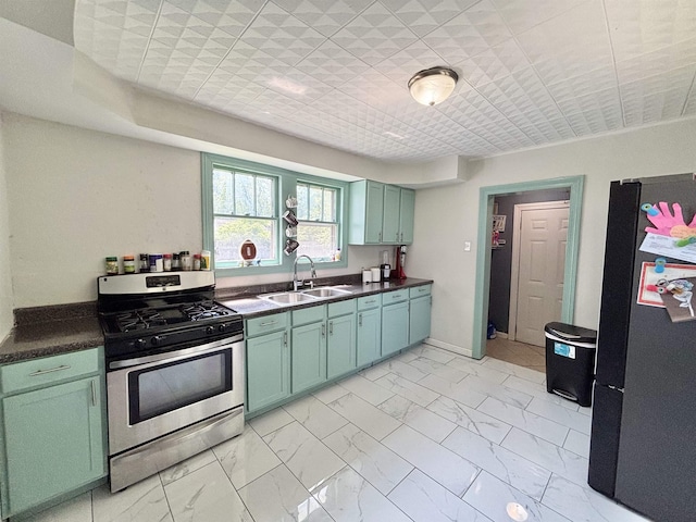 kitchen featuring dark countertops, a sink, stainless steel gas stove, marble finish floor, and freestanding refrigerator