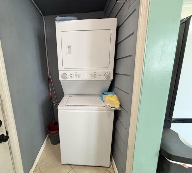 clothes washing area with stacked washer and dryer, laundry area, light tile patterned floors, and baseboards
