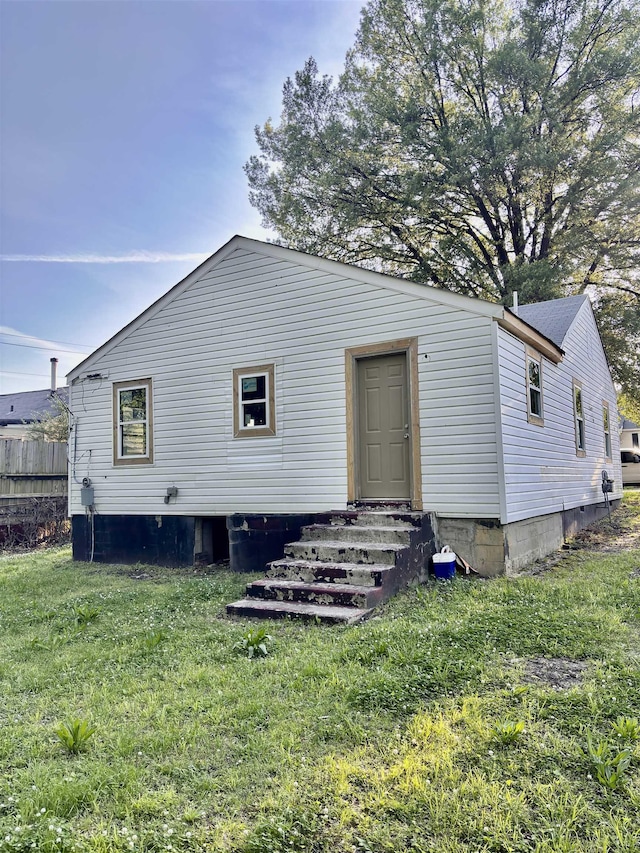 rear view of house with entry steps, fence, a lawn, and crawl space
