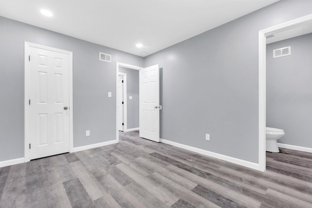 unfurnished bedroom featuring baseboards, ensuite bath, wood finished floors, and visible vents