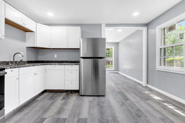 kitchen with white cabinets, light wood finished floors, freestanding refrigerator, dark stone counters, and baseboards