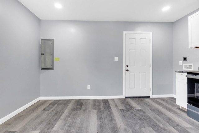 interior space featuring electric panel, wood finished floors, baseboards, white cabinets, and electric stove