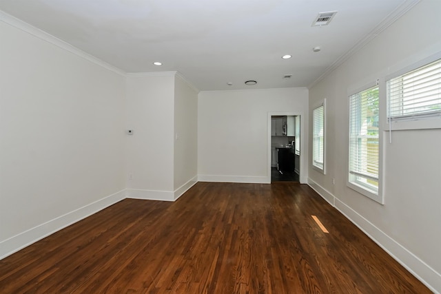 empty room featuring baseboards, dark wood finished floors, ornamental molding, and visible vents